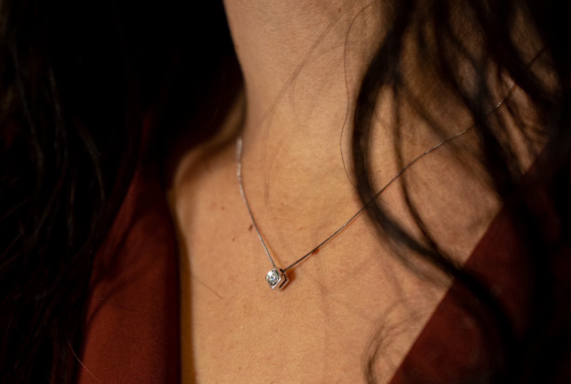 Collana in oro bianco con ciondolo a rombo impreziosito da un diamante, indossata da una donna