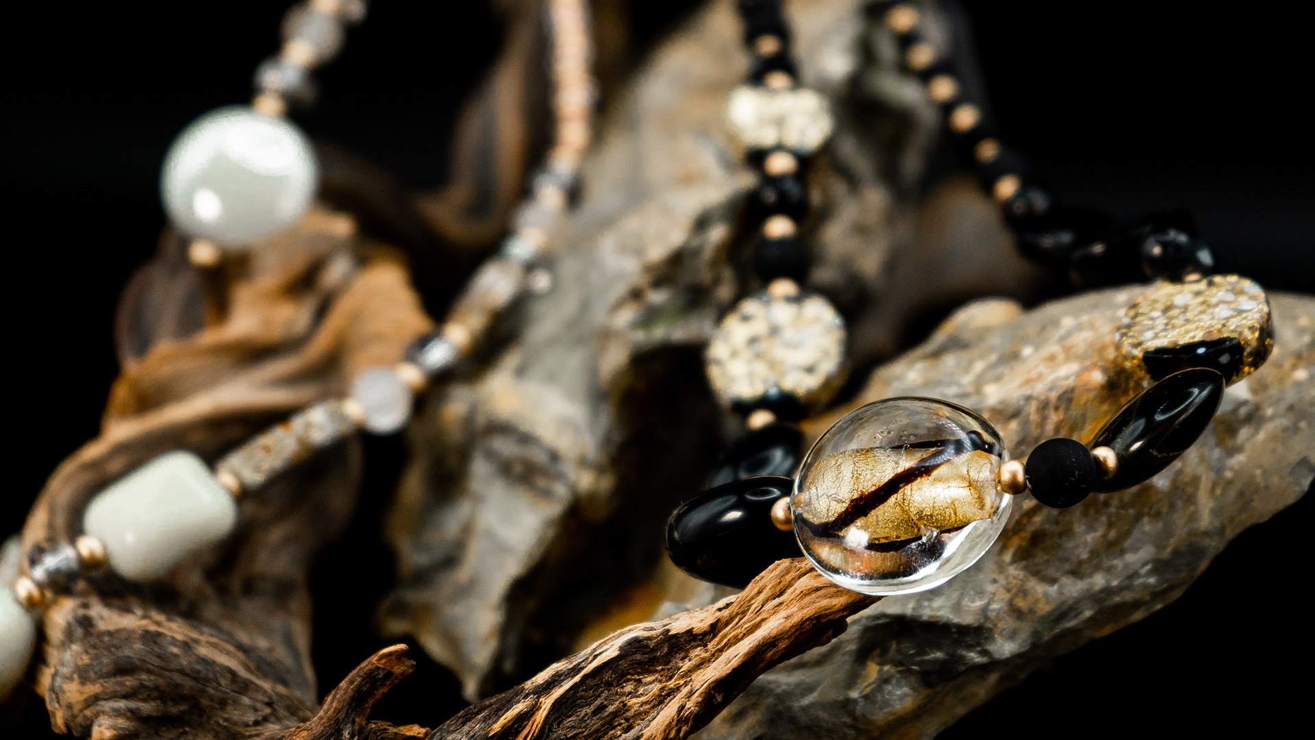 Collana Antica Murrina con perle in vetro di Murano nere, bianche e con foglia d'oro, appoggiata su legno e pietra