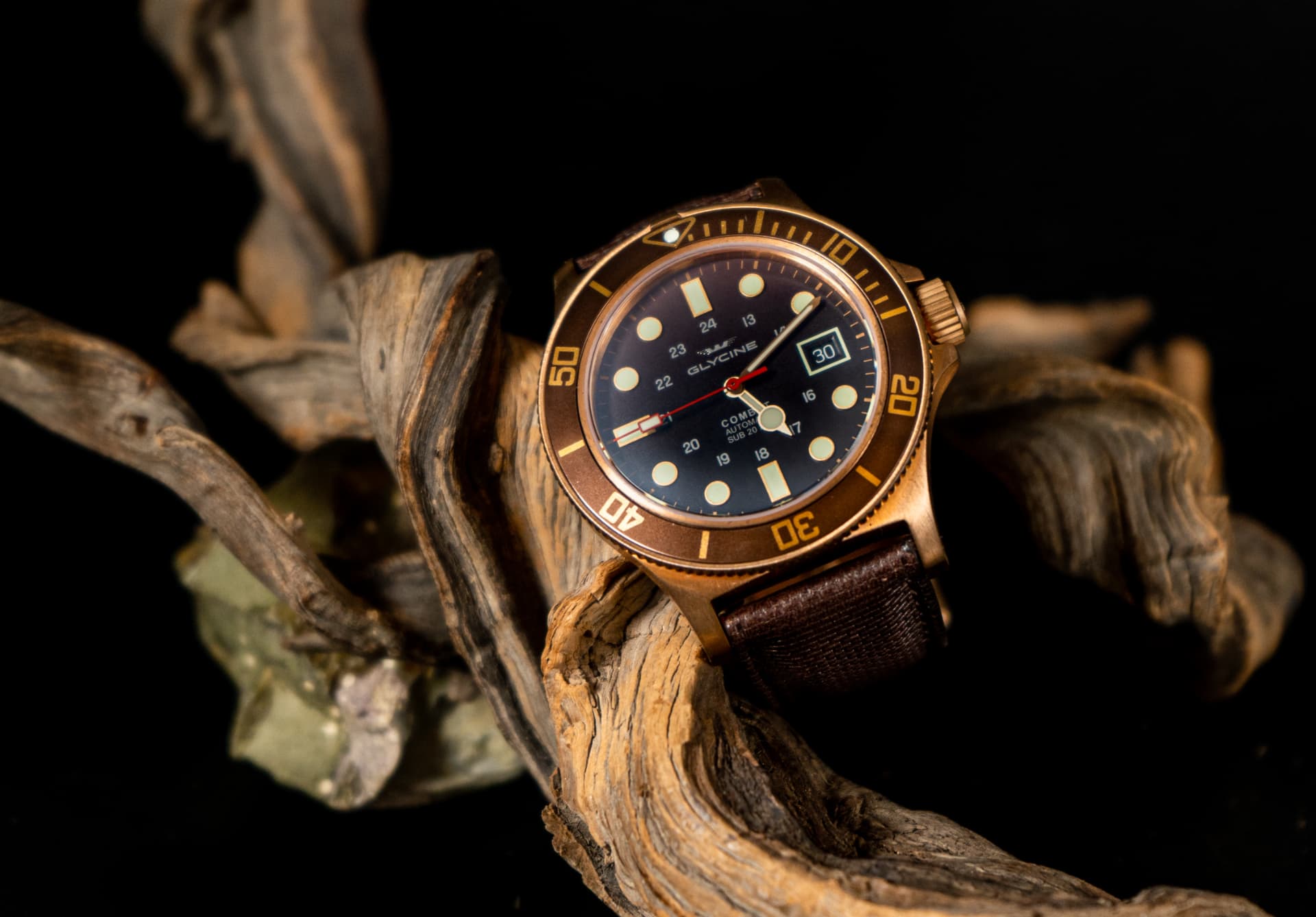 Orologio subacqueo automatico con cassa in bronzo e quadrante marrone, appoggiato su un legno naturale